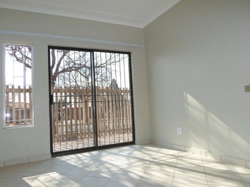 A bright, empty living area featuring neutral tiled flooring, coved ceilings, and a sliding glass door with integrated security bars leading outdoors.