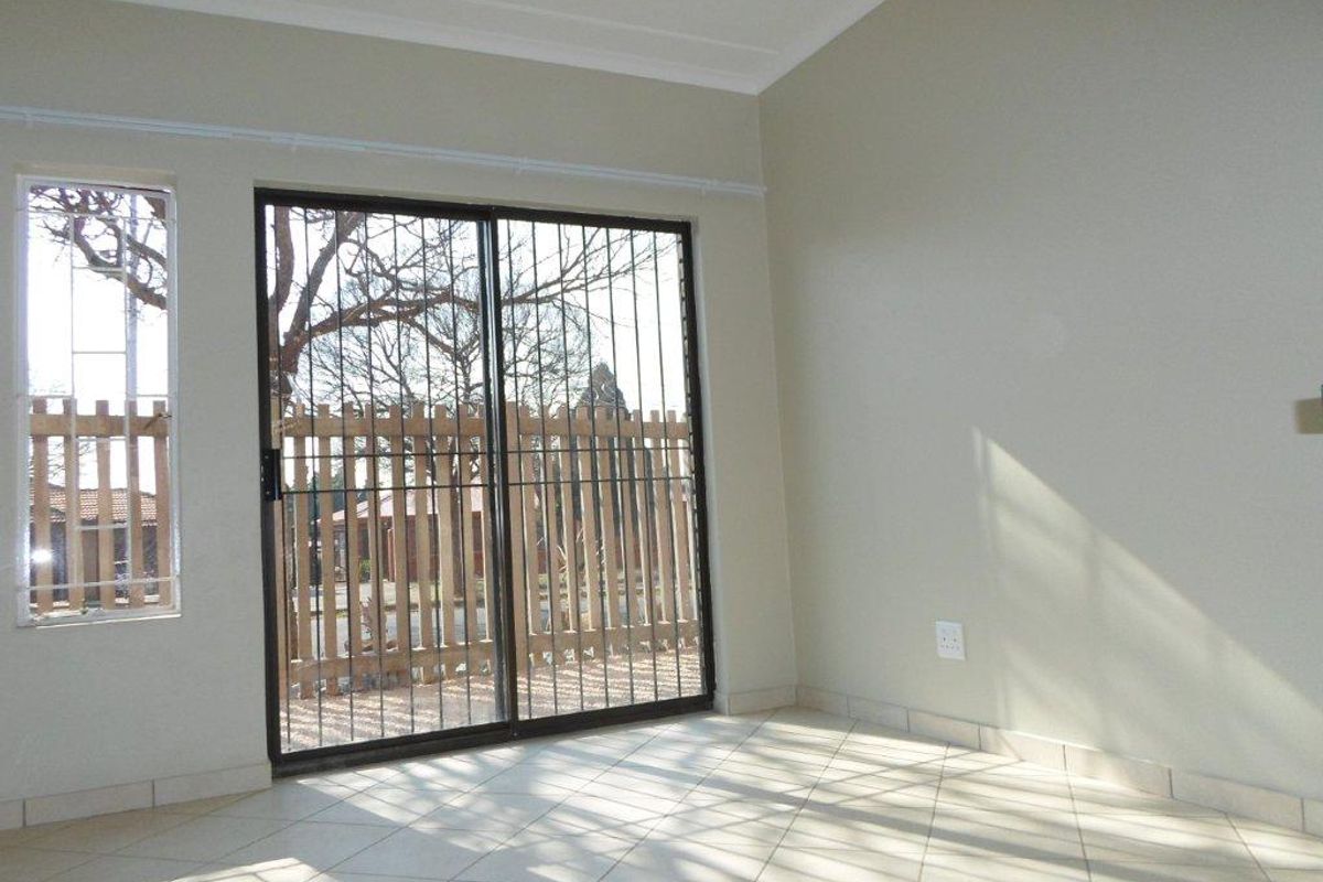 A bright, empty living area featuring neutral tiled flooring, coved ceilings, and a sliding glass door with integrated security bars leading outdoors.