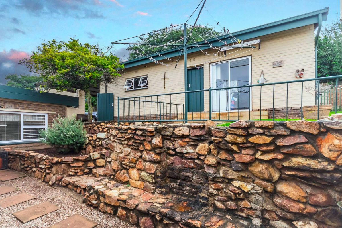 Rear view of the house featuring a stone retaining wall, raised patio area with metal railing, and sliding glass door access.