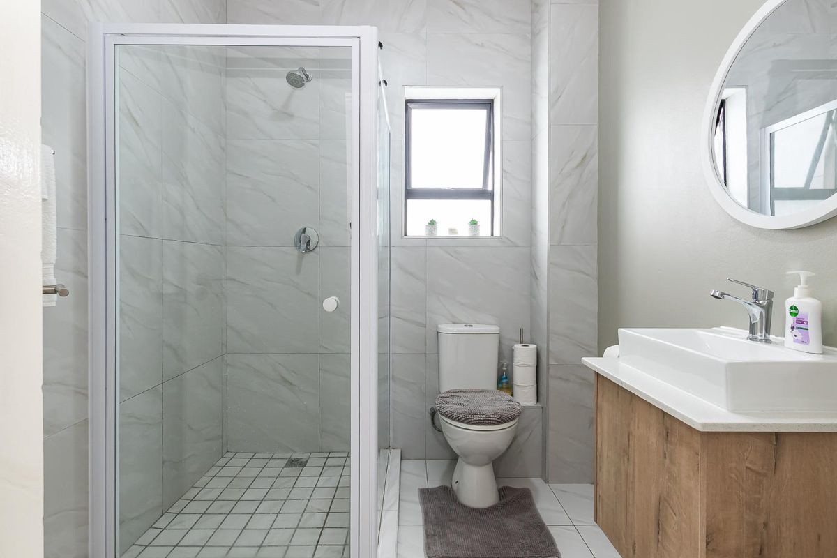 Modern bathroom featuring a glass-enclosed shower, a contemporary vanity with a vessel sink, and neutral marble-look wall tiling.