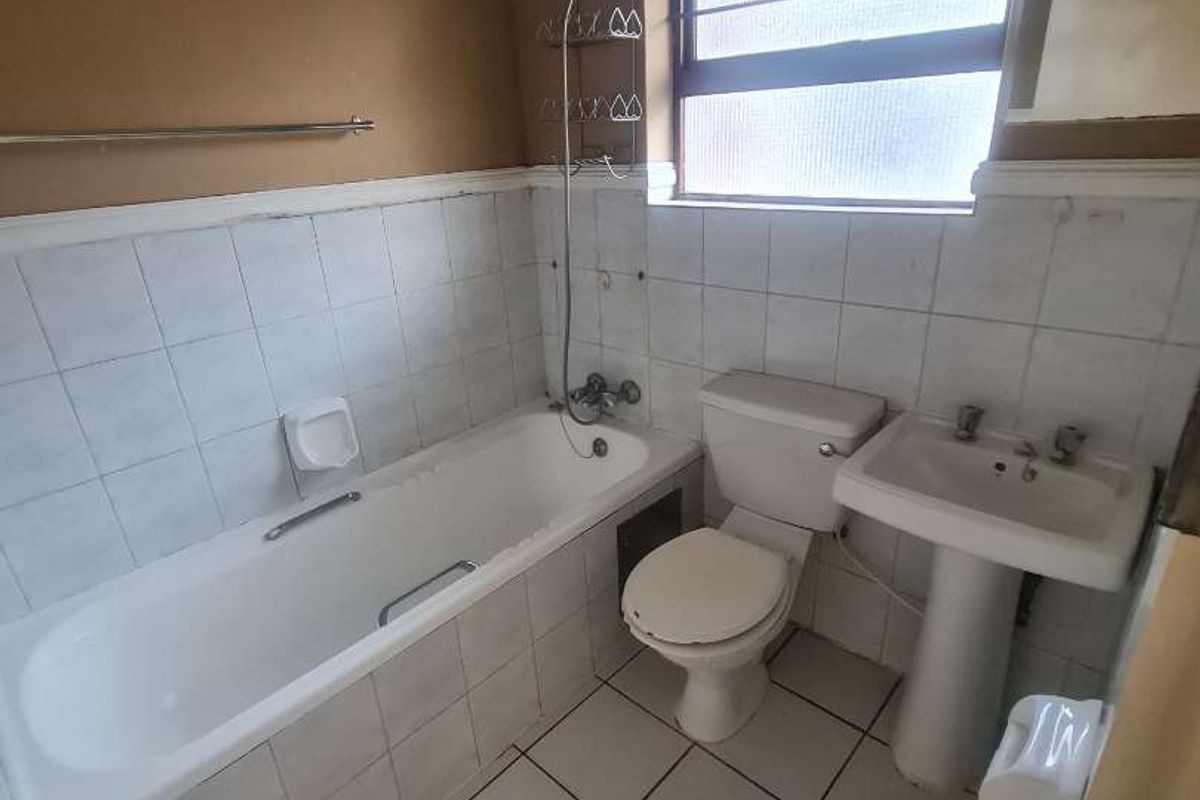 A dated bathroom featuring a standard bathtub, pedestal basin, and toilet with tiled walls and flooring, requiring cosmetic updates.