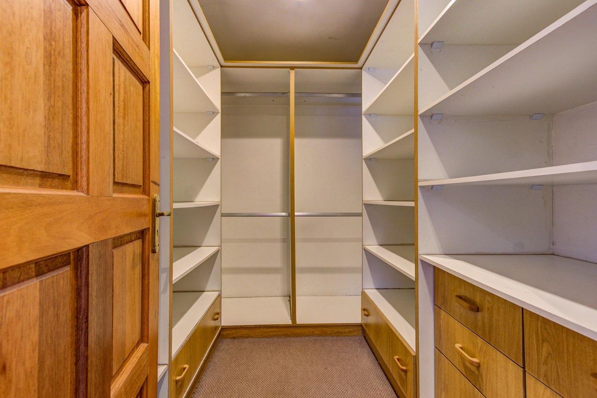 A walk-in closet featuring extensive built-in timber cabinetry, shelving, and hanging space, providing ample storage organization.
