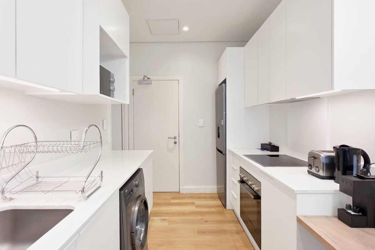 Modern galley-style kitchen featuring sleek white cabinetry, quartz countertops, integrated appliances, and light wood-look flooring in a clean, contemporary design.