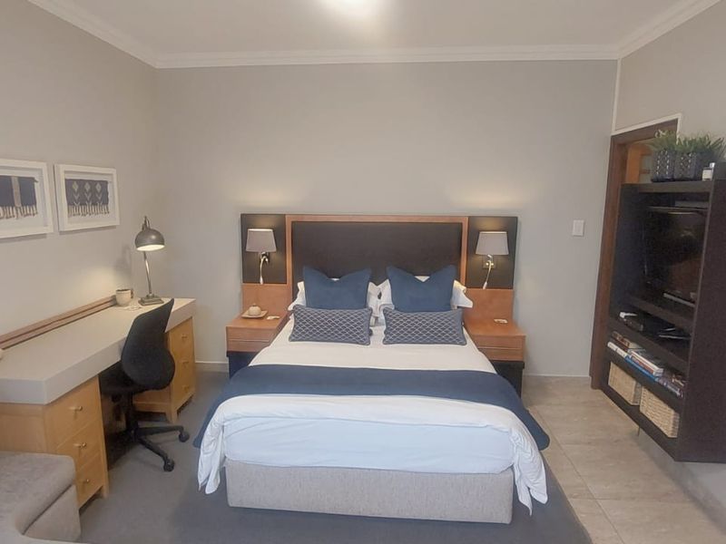 A well-maintained bedroom featuring a built-in headboard, integrated desk workspace, and custom shelving unit with tiled flooring and neutral wall finishes.