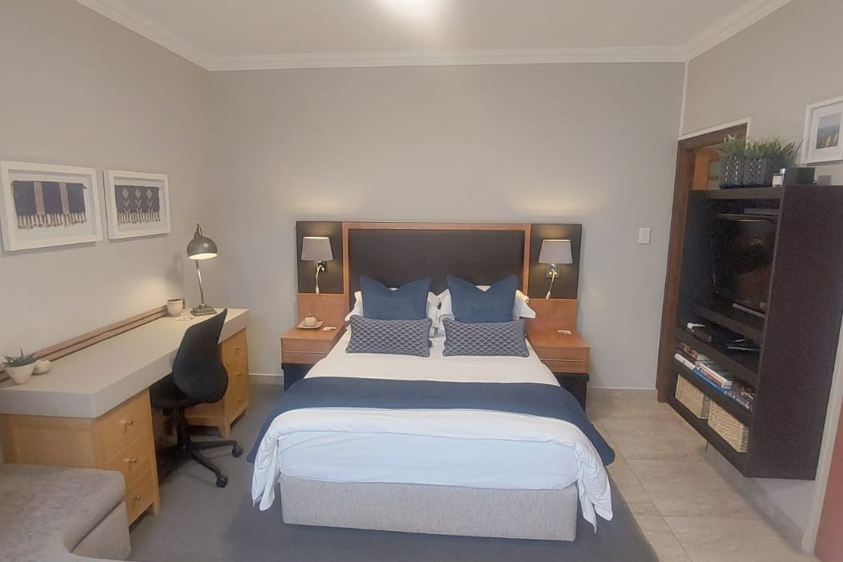 A well-maintained bedroom featuring a built-in headboard, integrated desk workspace, and custom shelving unit with tiled flooring and neutral wall finishes.