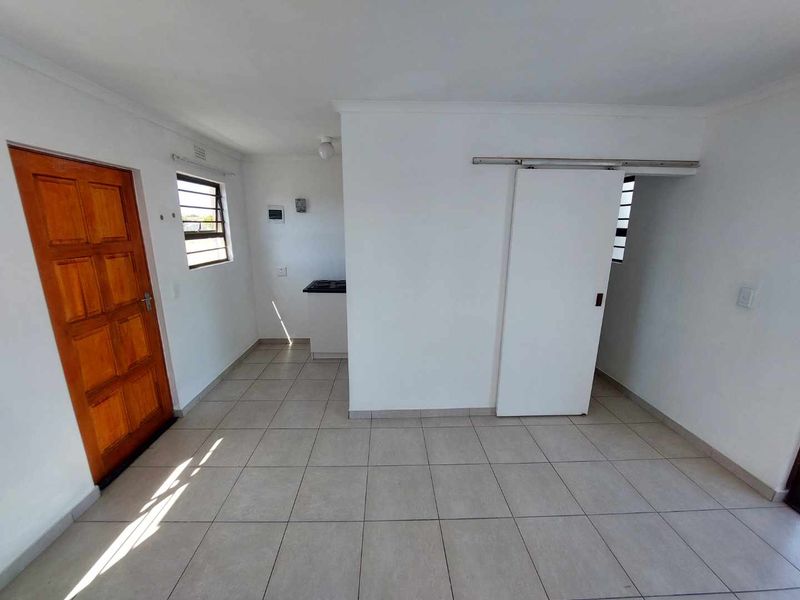 An open-plan living area featuring tiled flooring, a timber entrance door, and a compact kitchen corner with a built-in hob.