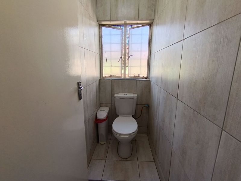 A compact, fully tiled guest toilet featuring neutral ceramic finishes and a small casement window for natural light.