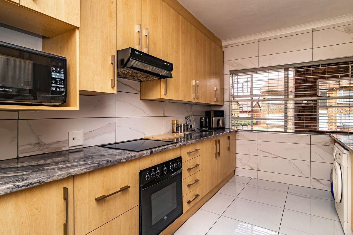 Modern kitchen featuring light wood cabinetry, dark stone countertops, marble-look wall tiling, and integrated appliances including an oven, hob, and microwave.