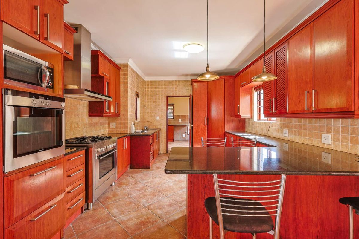 Spacious kitchen featuring warm-toned wooden cabinetry, granite countertops, a built-in oven, gas hob, stainless steel extractor fan, and a breakfast bar island.