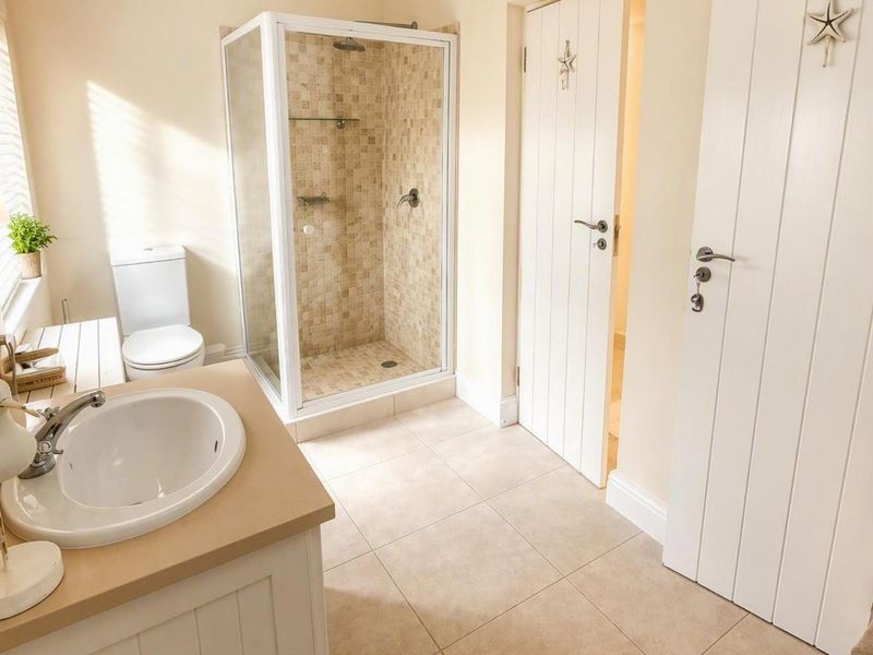 A bright and well-maintained bathroom featuring a glass-enclosed shower with mosaic tiling, a vanity basin, and neutral floor tiles.