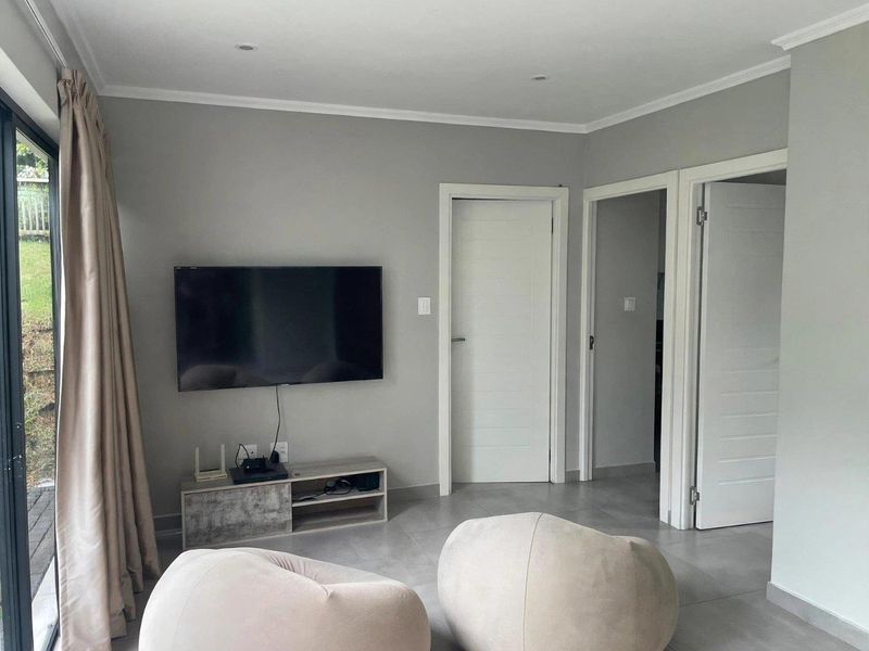A modern living room featuring neutral grey walls, tiled flooring, recessed downlights, and a sliding glass door providing access to the exterior.