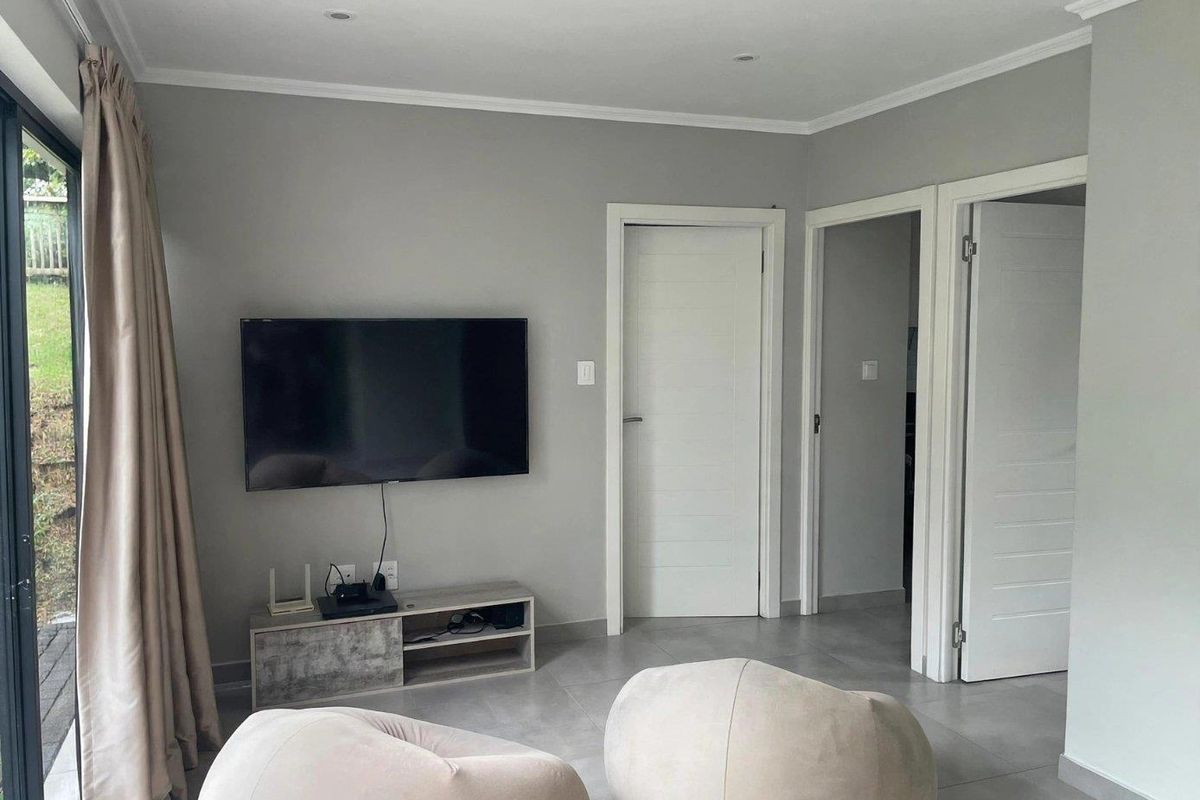 A modern living room featuring neutral grey walls, tiled flooring, recessed downlights, and a sliding glass door providing access to the exterior.