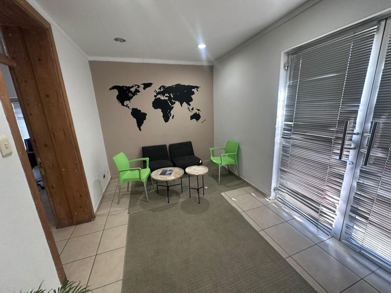 A functional office waiting area featuring tiled flooring, recessed lighting, and a large glass door with integrated blinds for natural light control.