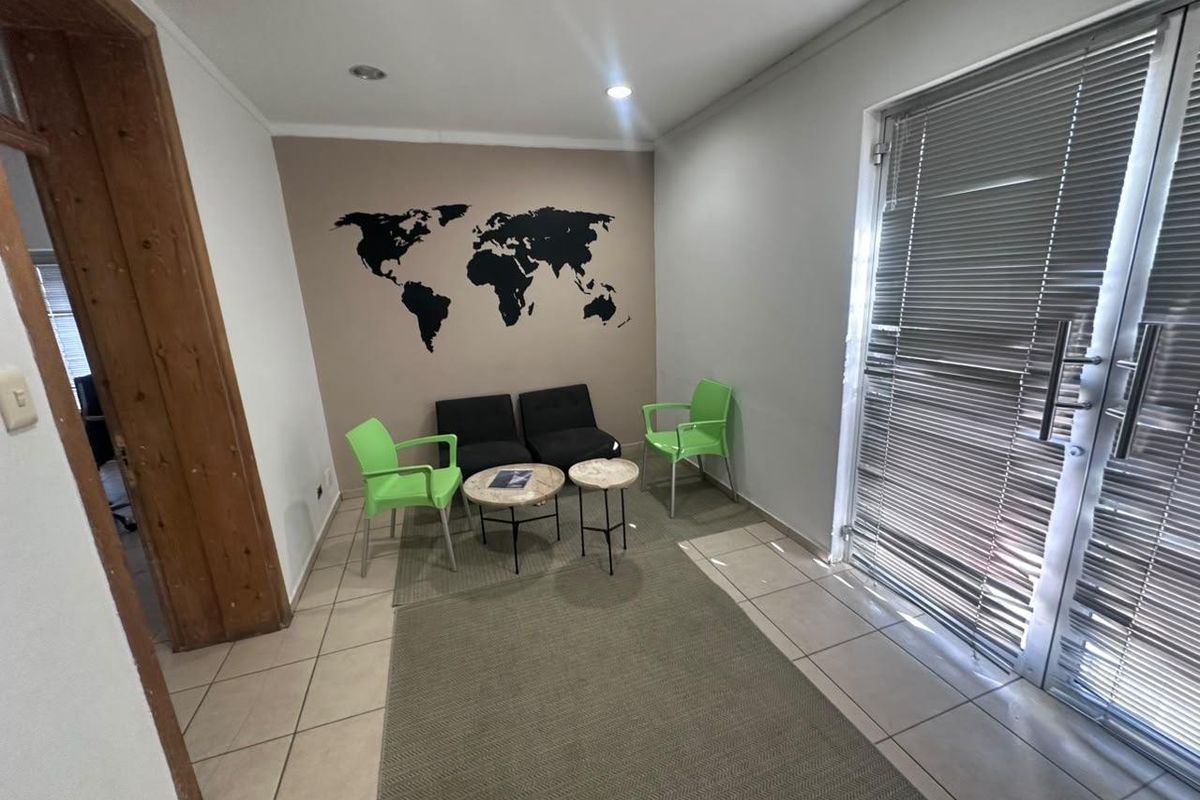 A functional office waiting area featuring tiled flooring, recessed lighting, and a large glass door with integrated blinds for natural light control.