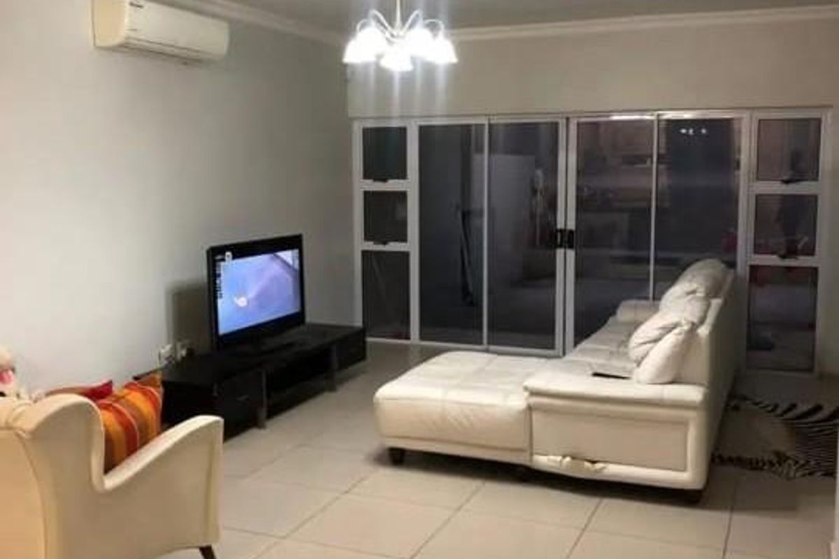 A spacious living room featuring large glass sliding doors, tiled flooring, and a wall-mounted air conditioning unit.