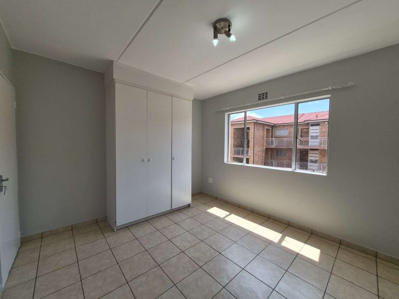 A bright, empty bedroom featuring neutral tiled flooring, a built-in wardrobe, and a large window providing natural light.
