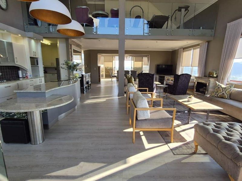 Spacious open-plan living area featuring a modern kitchen with stone island, mezzanine level with glass balustrade, and a cozy fireplace with scenic views.