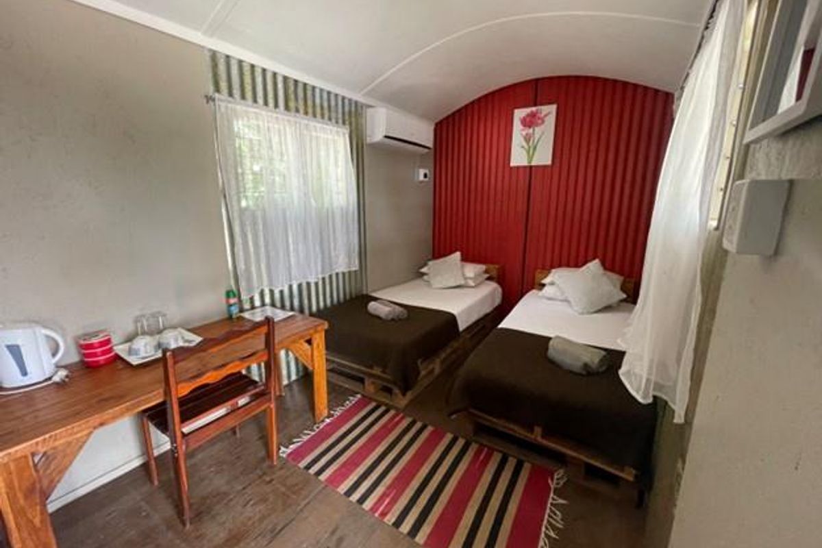 A compact bedroom featuring twin beds, a wall-mounted air conditioning unit, and corrugated metal wall accents.