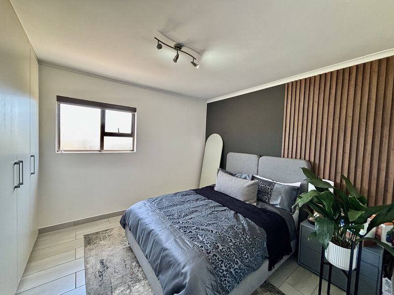 A well-maintained bedroom featuring built-in cupboards, a modern slatted wood accent wall, tiled flooring, and contemporary track lighting.