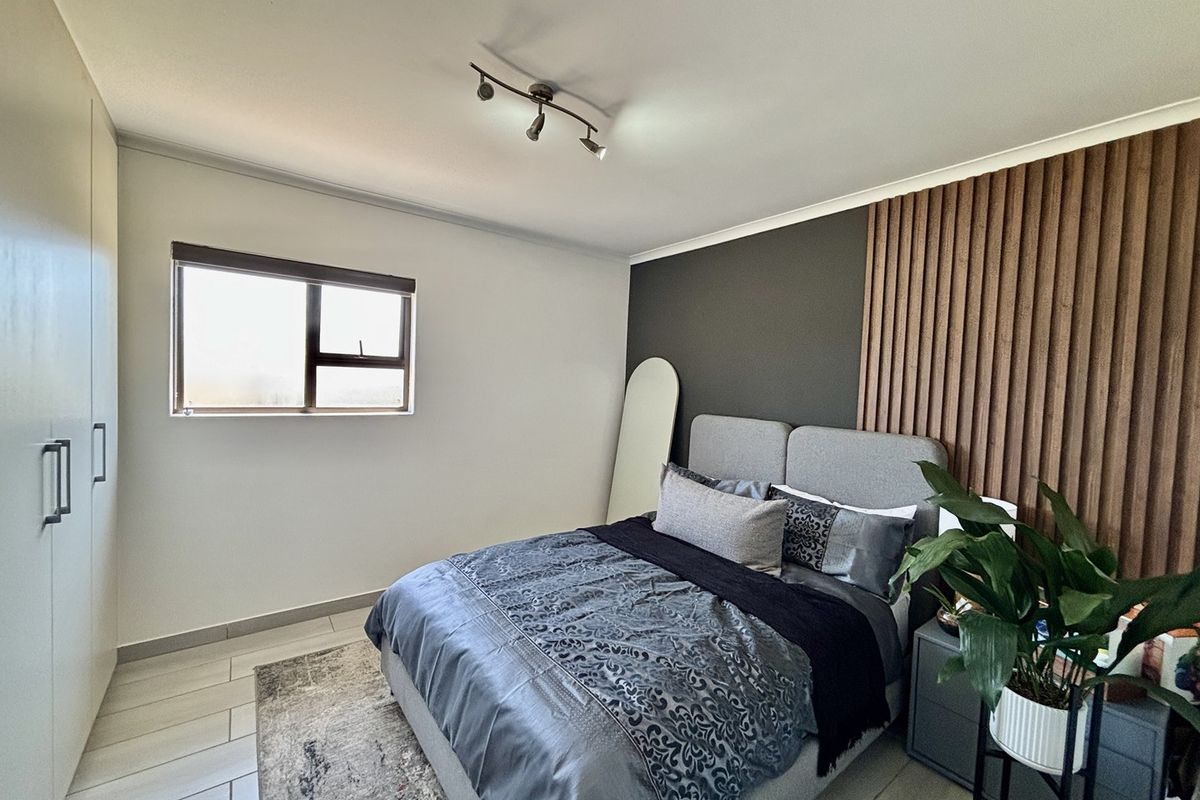 A well-maintained bedroom featuring built-in cupboards, a modern slatted wood accent wall, tiled flooring, and contemporary track lighting.