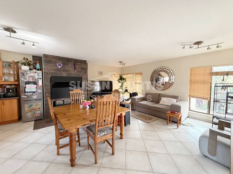 Open-plan living and dining area featuring tiled flooring, a stone-clad built-in fireplace, and large windows with venetian blinds.