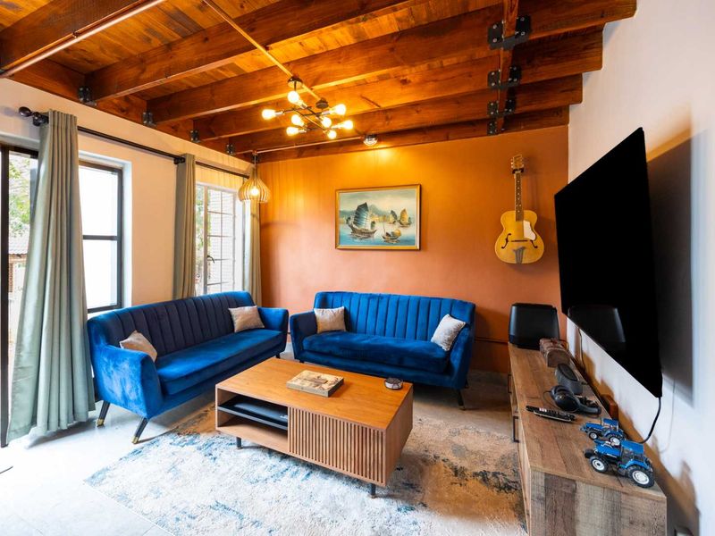 A cozy living room featuring exposed timber ceiling beams, copper piping accents, and large glass sliding doors that provide ample natural light.