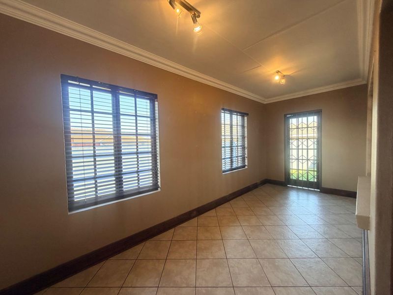 An empty living area featuring tiled flooring, security gate access, and neutral wall tones, providing a versatile space ready for personalization.