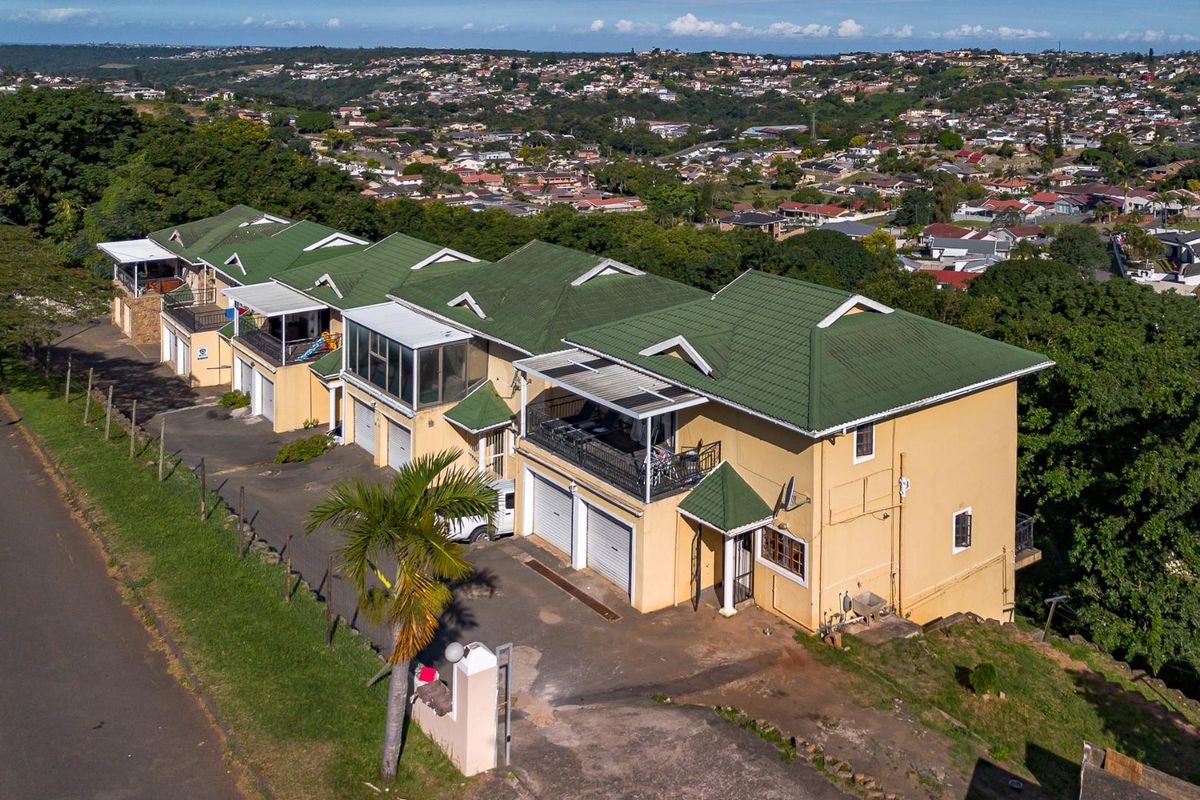 Aerial view of a townhouse complex featuring green tiled roofs, multiple garage doors, and elevated balconies overlooking the surrounding residential area.