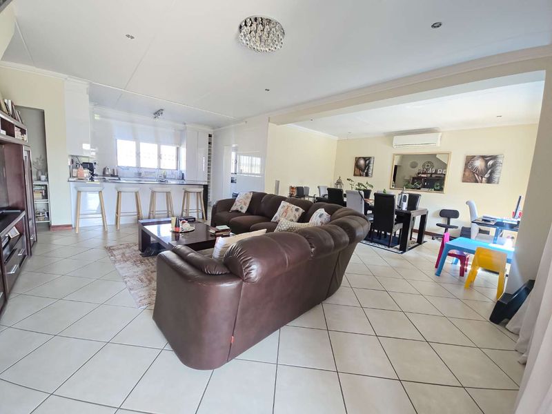 Spacious open-plan living area featuring a modern kitchen with island, dining space, and tiled flooring throughout, creating a functional and connected family environment.