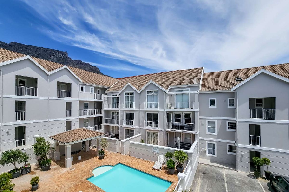 Aerial view of an apartment complex featuring a central swimming pool, paved courtyard, covered gazebo, and multiple residential balconies with mountain views.