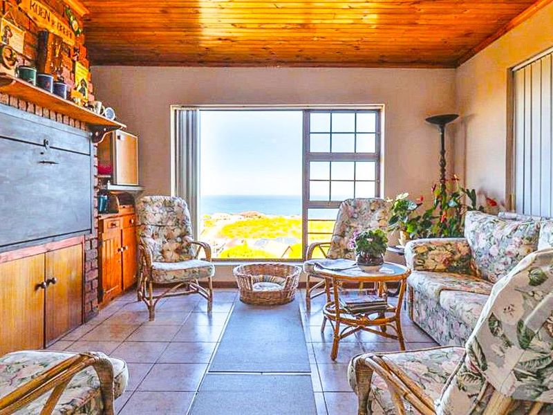 A living room featuring a brick fireplace, timber ceiling, and tiled flooring, with a large window offering scenic coastal views.