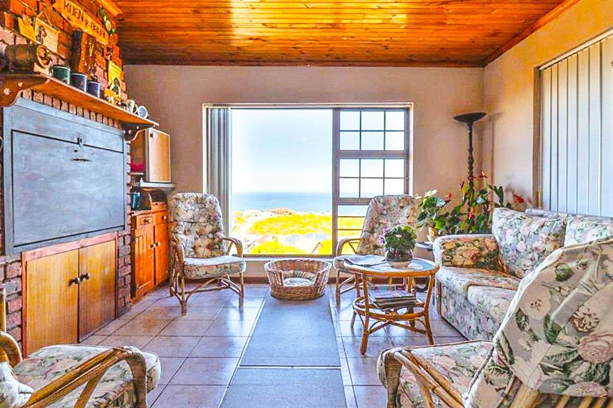 A living room featuring a brick fireplace, timber ceiling, and tiled flooring, with a large window offering scenic coastal views.