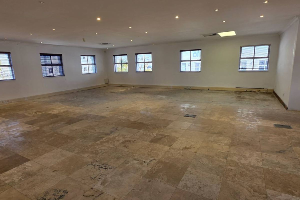 Spacious open-plan office area featuring natural stone tile flooring, recessed downlighting, and multiple windows providing ample natural light.