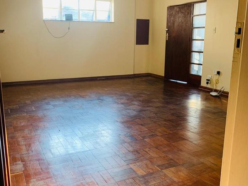 An empty living room featuring original parquet flooring, a ceiling fan, and a timber entrance door with side glazing.