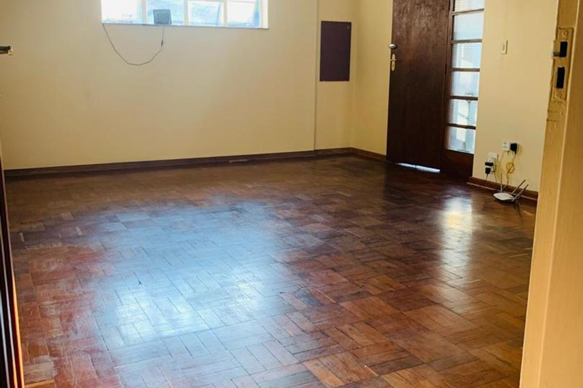 An empty living room featuring original parquet flooring, a ceiling fan, and a timber entrance door with side glazing.