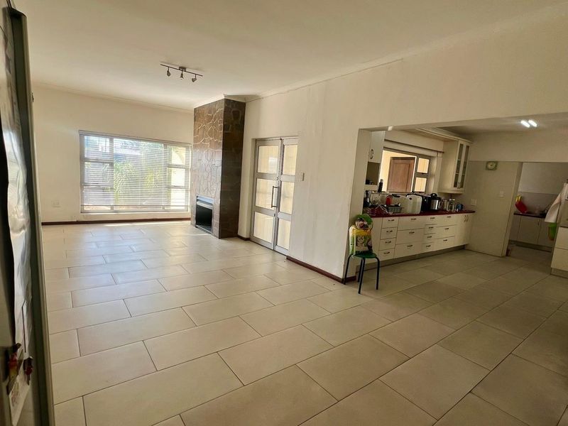 Open-plan living and kitchen area featuring large format floor tiles, a stone-clad fireplace, and functional kitchen cabinetry with ample storage space.