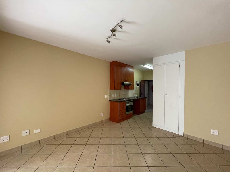 An open-plan living area featuring tiled flooring, a compact kitchen with built-in cabinetry, an electric hob, and an integrated oven.
