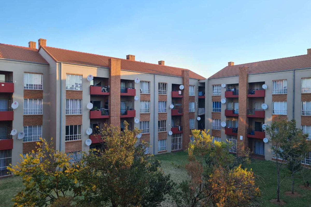Exterior view of a multi-story apartment complex featuring brick facade detailing, private balconies, and a shared communal garden area.