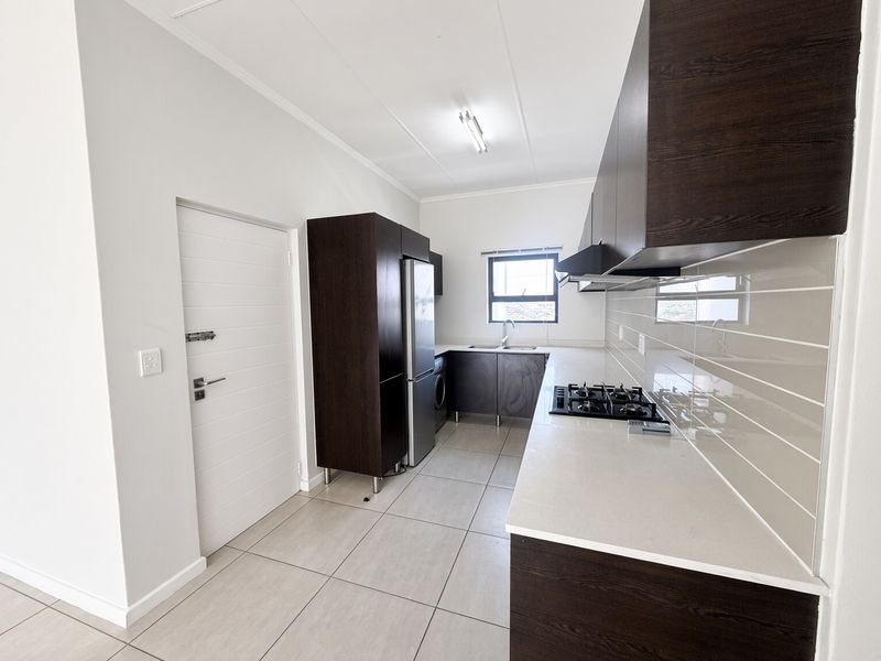 Modern kitchen featuring dark wood cabinetry, stone countertops, a gas hob with extractor fan, and neutral tiled flooring.