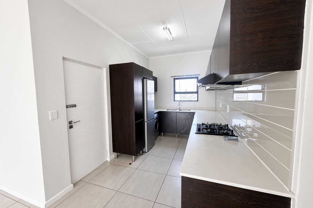 Modern kitchen featuring dark wood cabinetry, stone countertops, a gas hob with extractor fan, and neutral tiled flooring.