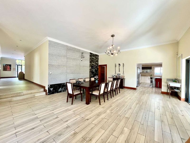 Spacious open-plan dining area featuring wood-look tile flooring, a striking stone feature wall, and elegant chandelier lighting, flowing seamlessly into the adjacent kitchen.