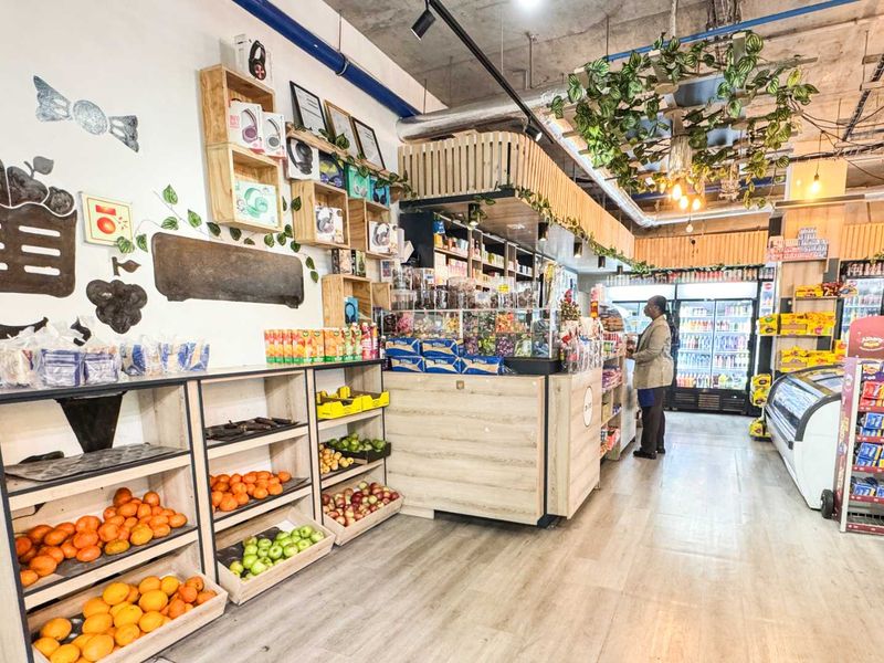 A well-maintained retail space featuring built-in wooden produce shelving, a central service counter, and commercial refrigeration units under an exposed industrial-style ceiling.