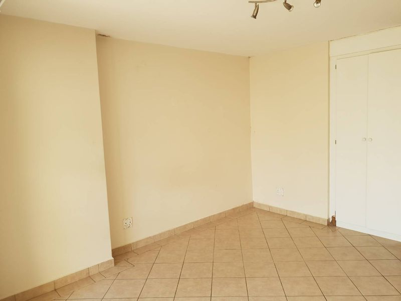 An empty bedroom featuring neutral wall paint, tiled flooring, and a built-in cupboard with some visible wear at the base.