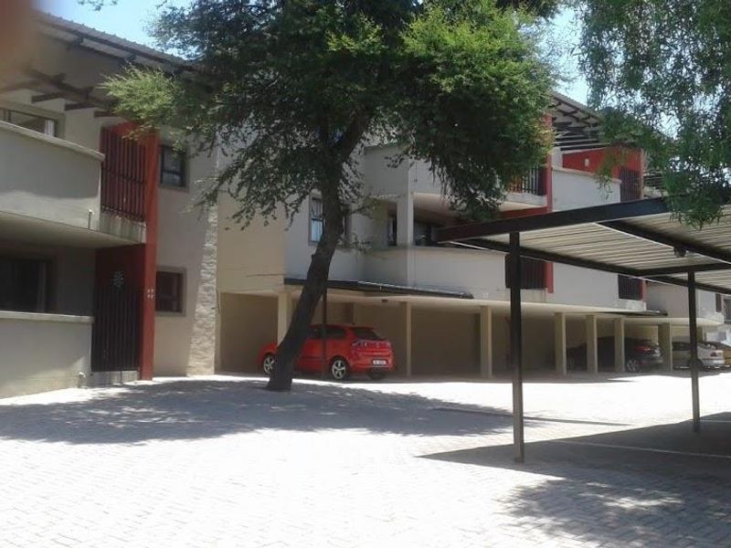 Exterior view of the apartment complex featuring covered parking bays, paved driveway, and balcony access for the residential units.