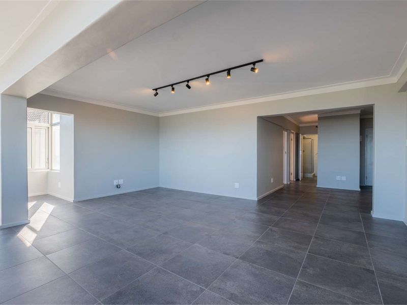 Spacious open-plan living area featuring modern grey floor tiles, neutral walls, and contemporary track lighting, offering a versatile layout for various living arrangements.