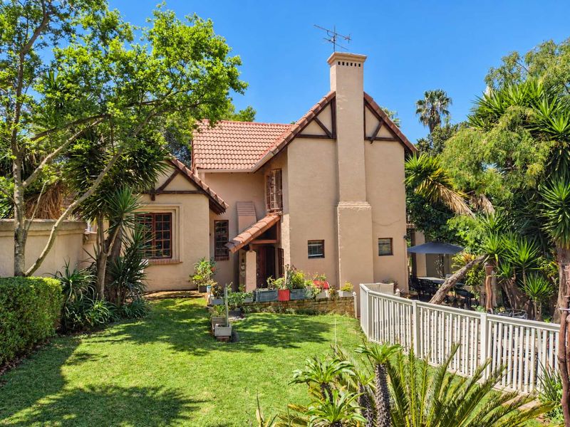 A well-maintained rear elevation of a house featuring a tiled roof, prominent chimney, and established garden with a picket fence.