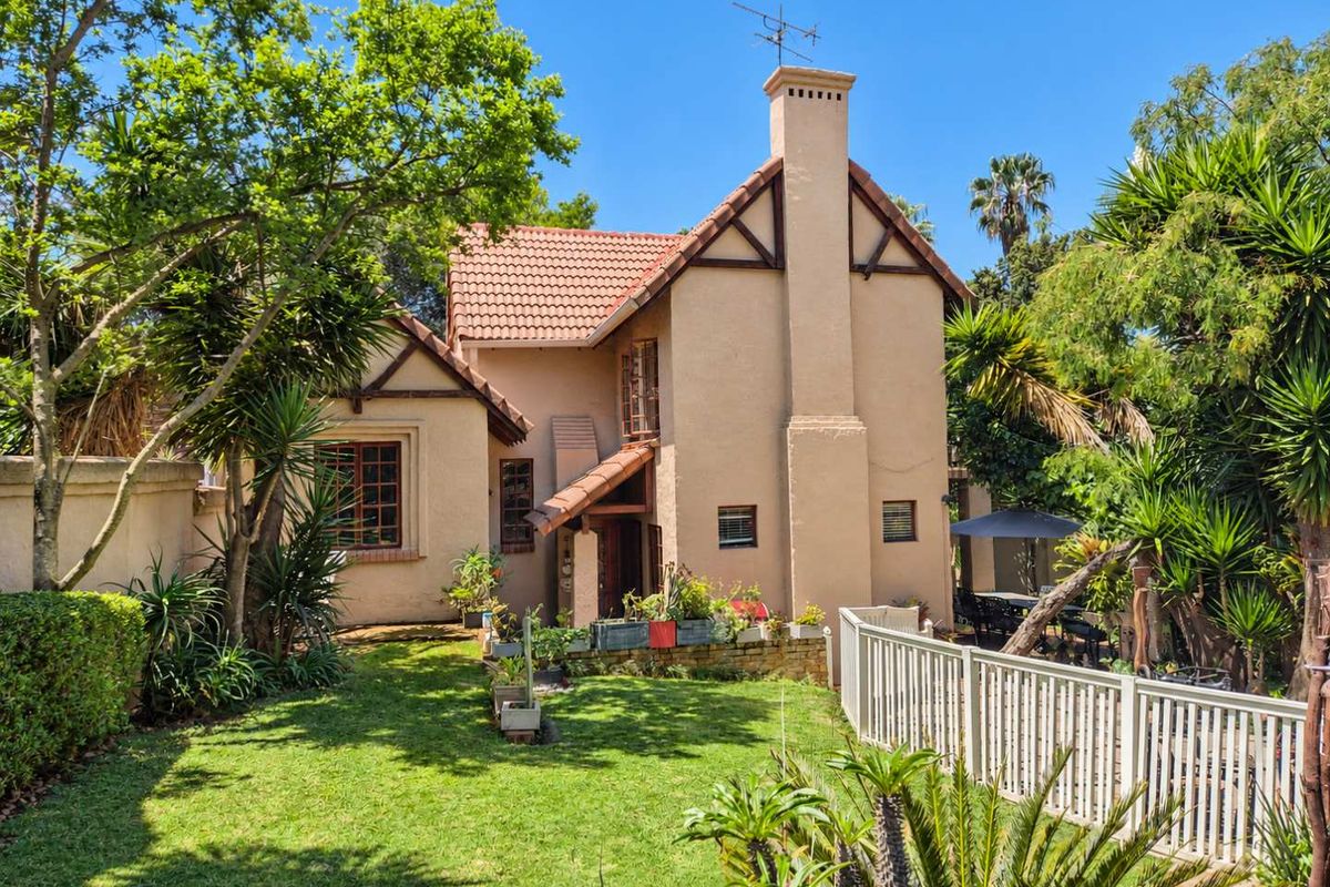 A well-maintained rear elevation of a house featuring a tiled roof, prominent chimney, and established garden with a picket fence.