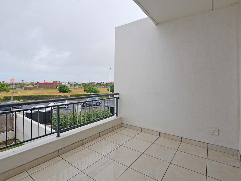 A clean, tiled balcony featuring a metal balustrade and an external power outlet, offering an open view of the surrounding area.