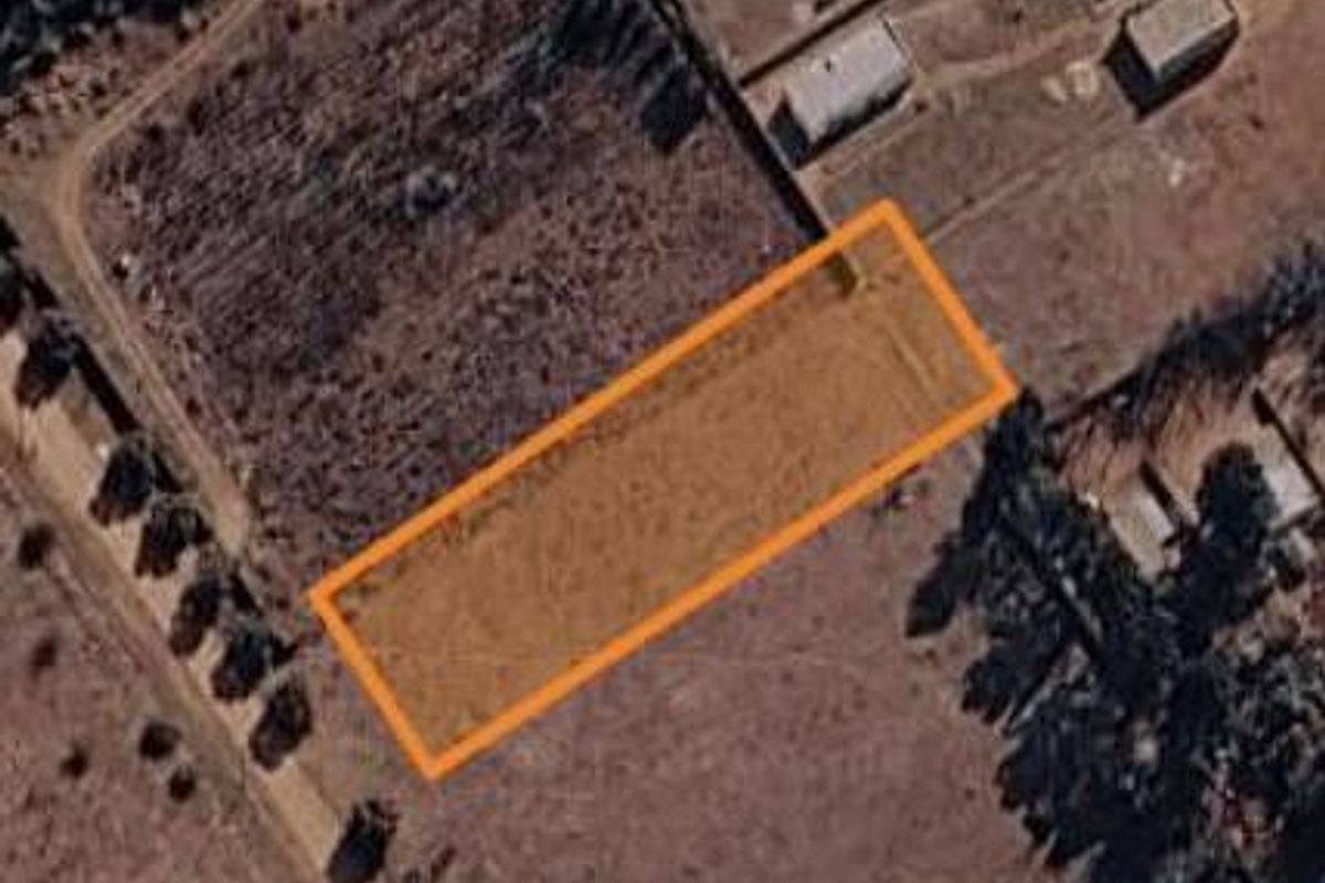 An aerial view of a vacant residential plot with an orange boundary overlay indicating the property lines.