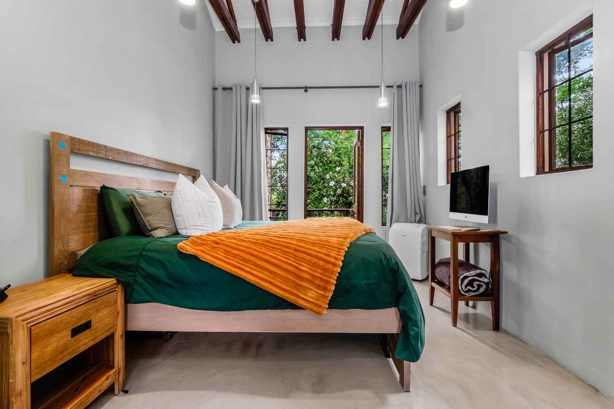 A bright bedroom featuring exposed timber ceiling beams, polished concrete flooring, and direct access to a private outdoor area through glass-paneled doors.